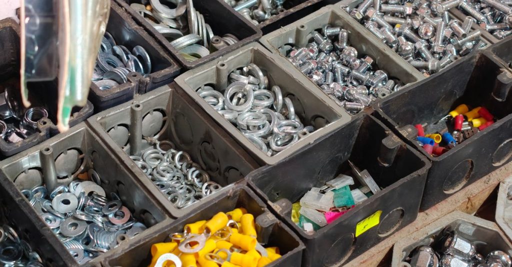 Close-up view of various hardware fasteners in black storage bins, including nuts, bolts, and washers.