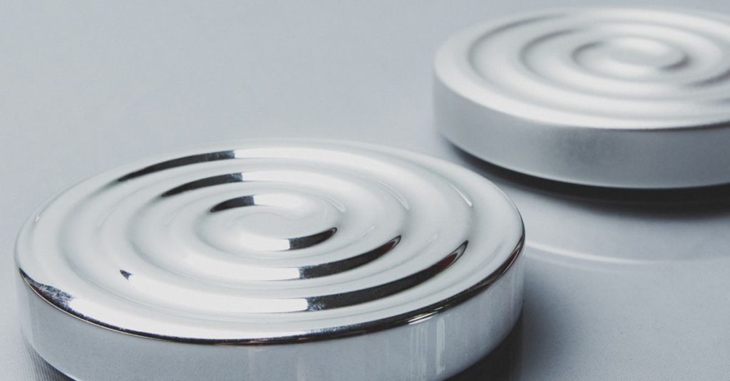 Two minimalist circular steel objects with concentric design on a reflective surface.
