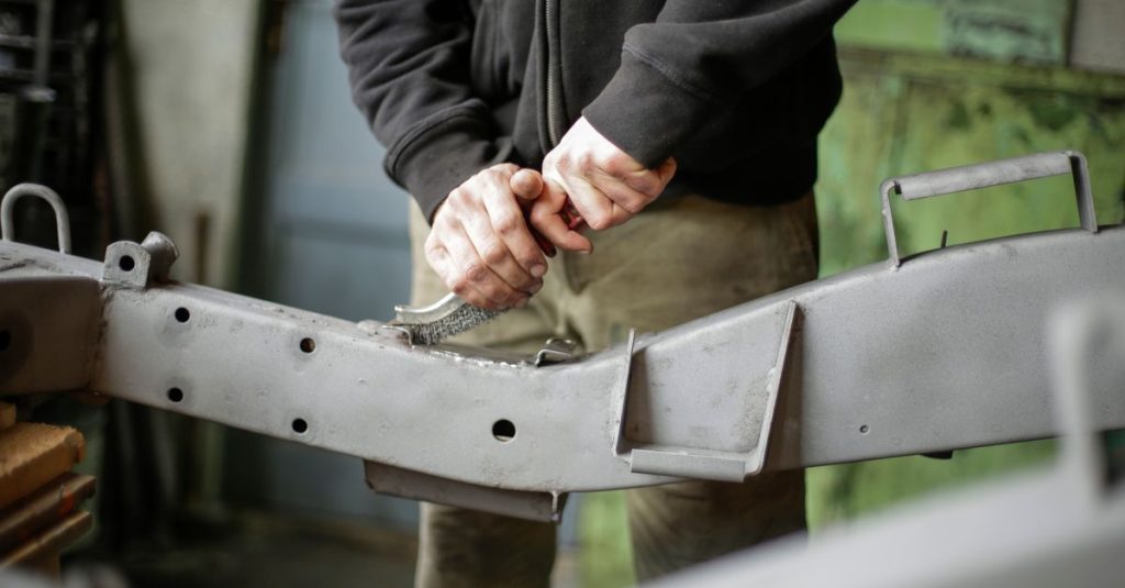 Pasinler Hurdacı Unrecognizable crop male mechanic standing near metal construction and scrubbing surface with metal brush while working in garage