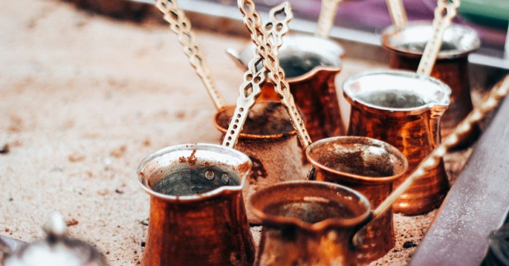 Close-up of traditional copper Turkish coffee pots placed on sand for brewing.